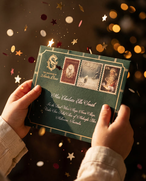 Personalised Letter From Santa Claus - A child holding an emerald green Santa letter envelope hand addressed in gold, with confetti stars falling around it