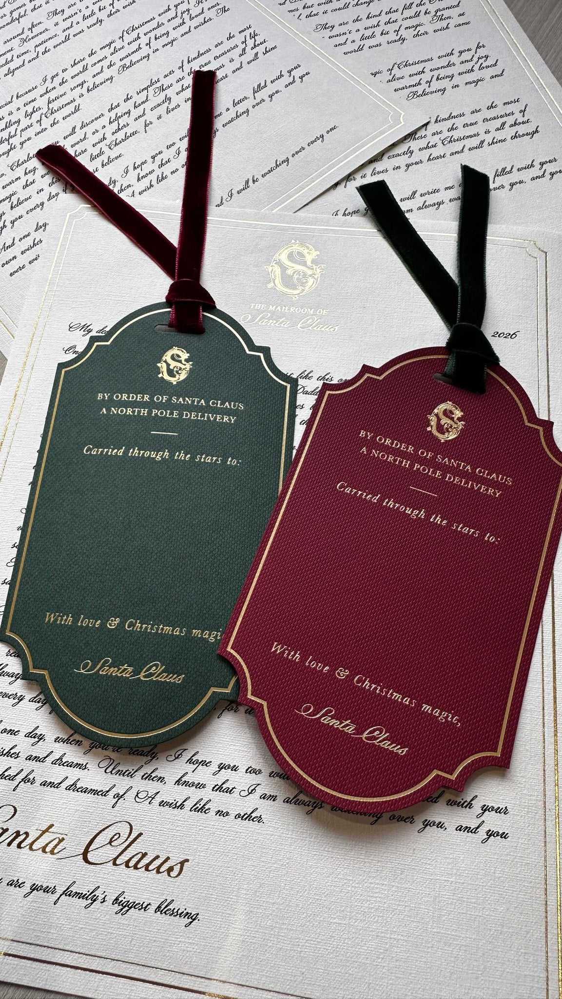 Large personalised Christmas gift tags in green and red with velvet ribbons, resting on letters from Santa