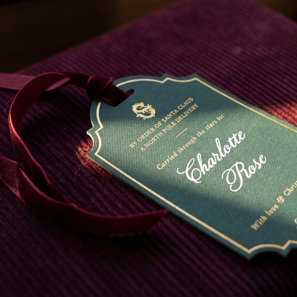 Large Personalised Christmas Gift Tag - A green personalised gift tag reading Charlotte Rose resting on the burgundy corduroy lid of the Christmas Eve Trunk